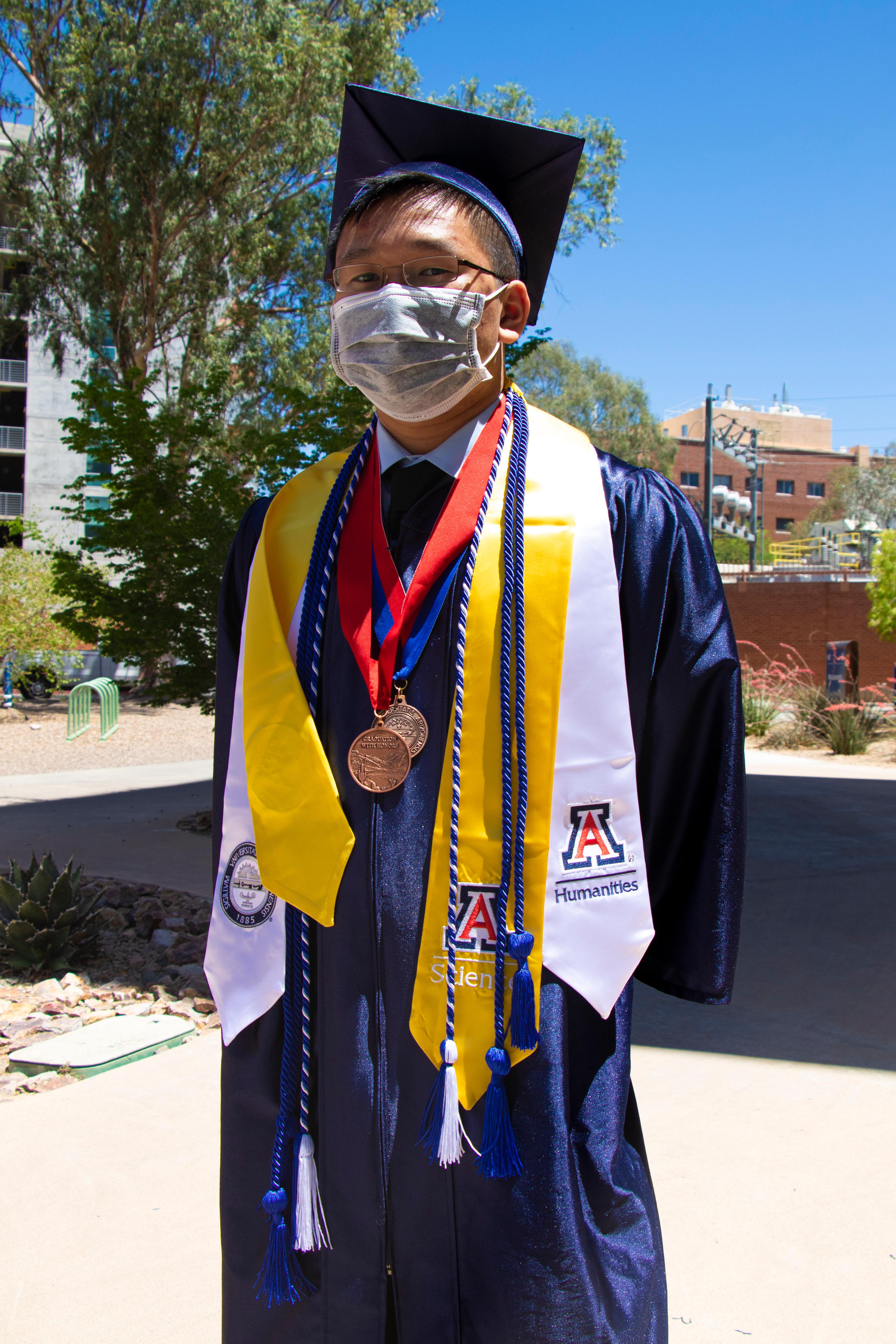 Ryan in graduation regalia with honors medals and a covid mask