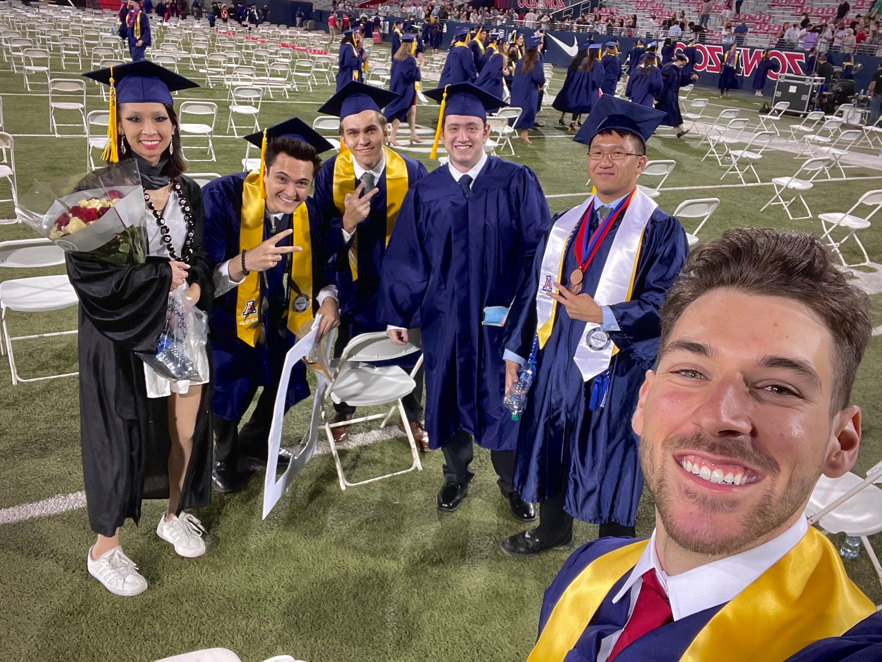 Selfie of Ryan and five friends in caps and gowns on the stadium field at the University of Arizona commencement