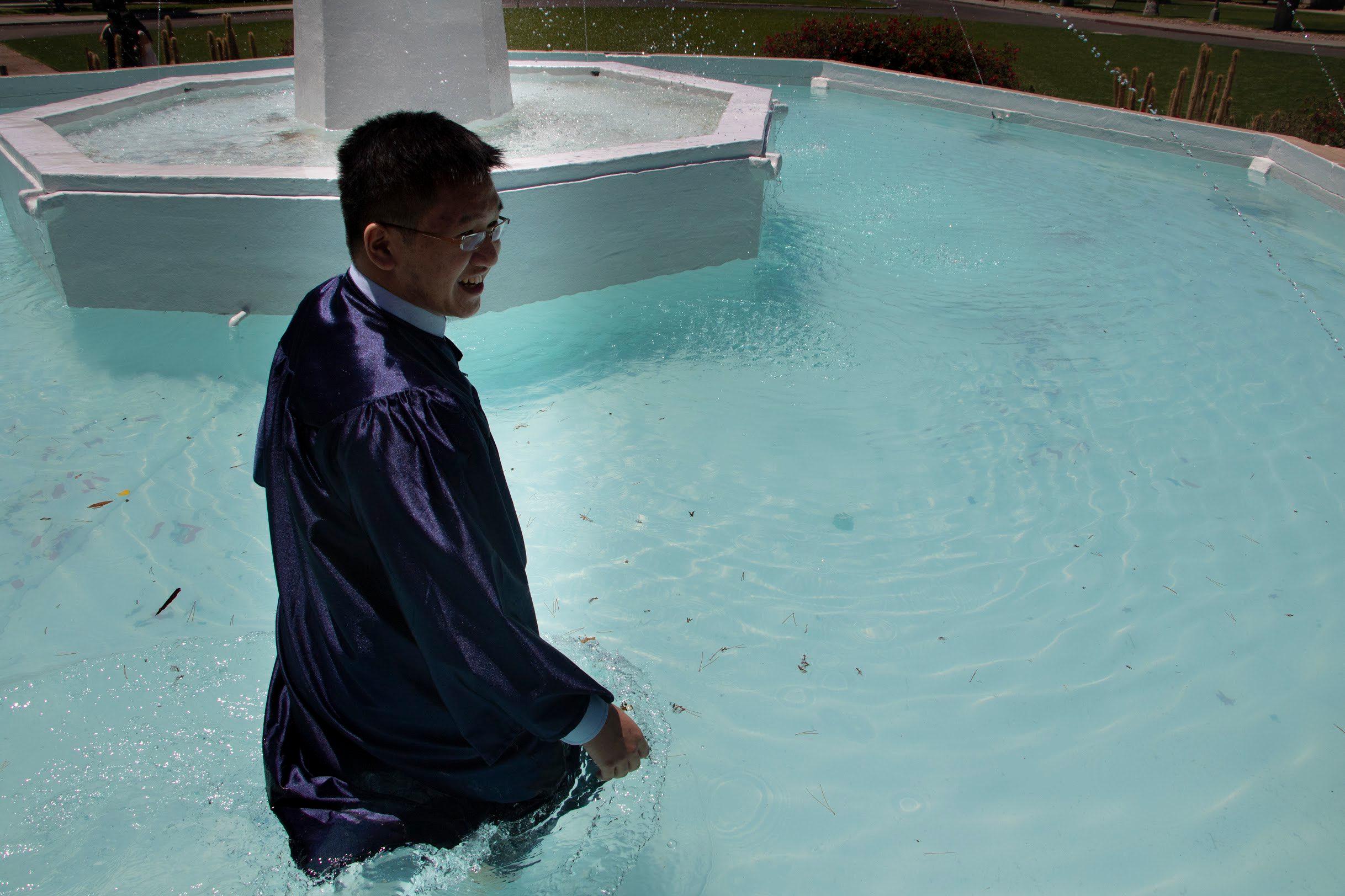 Ryan standing waist-deep in the Old Main fountain in his graduation gown, grinning