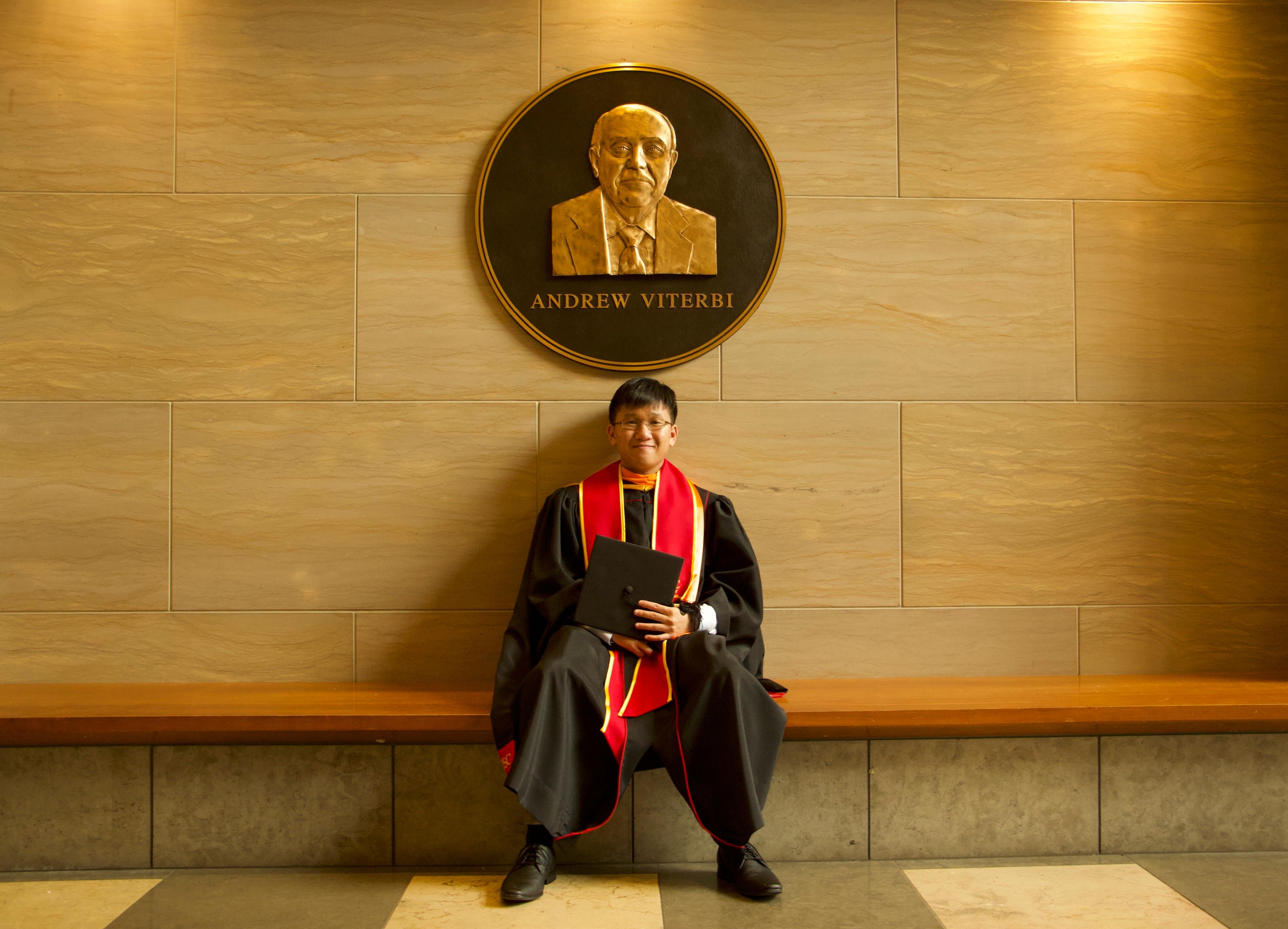 Ryan in his USC cap and gown seated beneath a bronze medallion portrait of Andrew Viterbi